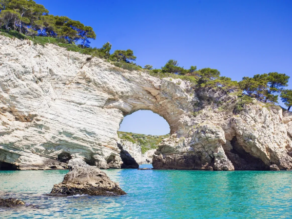 Scogliera bianca con arco naturale sul mare azzurro.