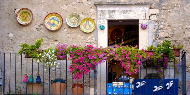 Balcone fiorito con piatti decorativi su un muro di pietra.