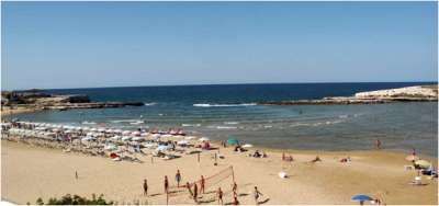 Spiaggia con ombrelloni, persone che giocano a pallavolo e mare calmo.