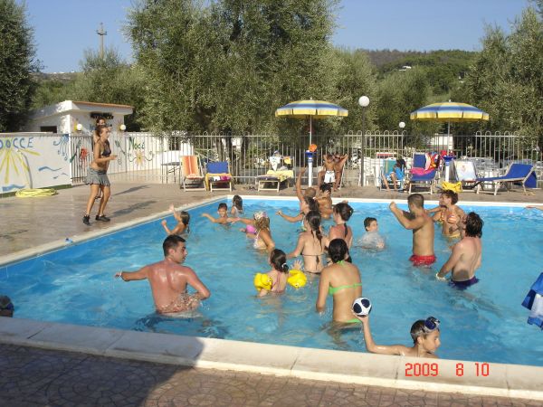 Gruppo di persone che giocano e nuotano in una piscina luminosa con ombrelloni intorno.