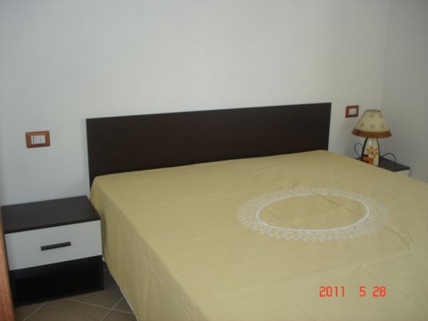 Camera da letto con letto matrimoniale e copriletto beige. Due comodini con lampade.