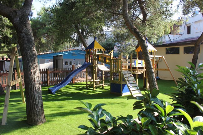 Parco giochi con erba sintetica, scivolo e altalene.