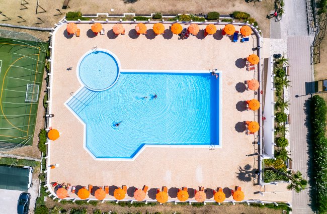 Piscina con ombrelloni arancioni vista dall'alto.