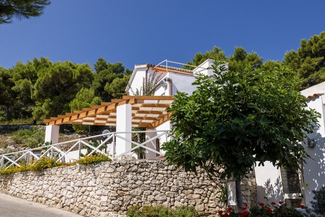 Villa bianca con pergolato di legno e giardino fiorito.