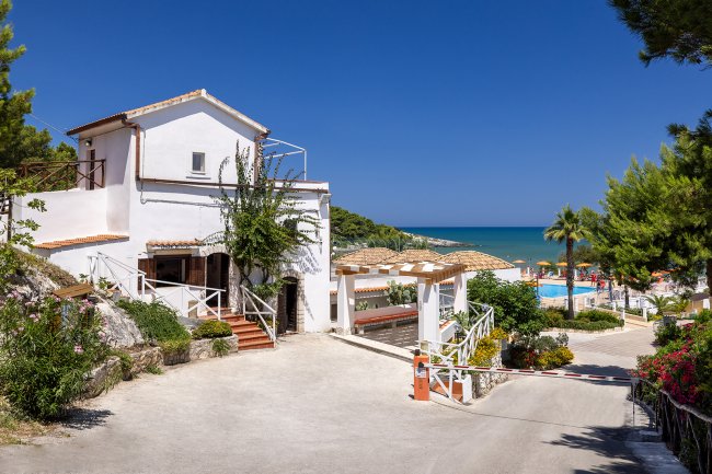 Edificio bianco su una collina con vista sul mare e piscina con ombrelloni arancioni.