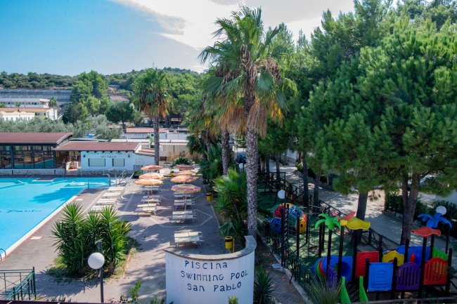 Piscina con ombrelloni, palme e area giochi, insegna 