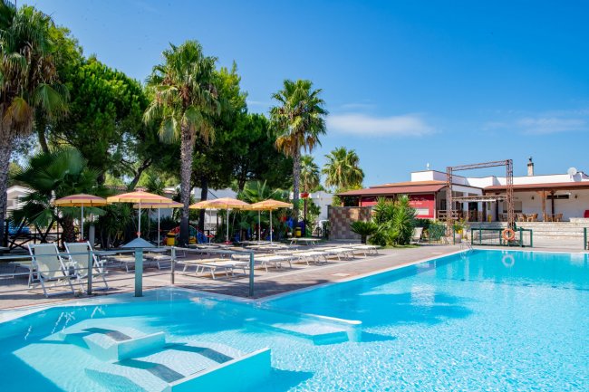 Piscina con lettini, ombrelloni e palme.