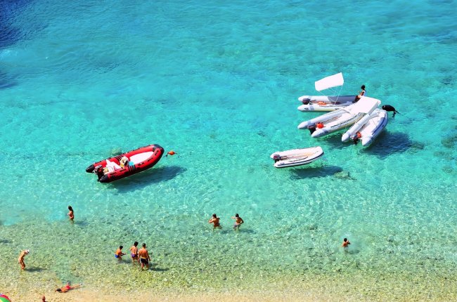 Mare cristallino con gommoni e bagnanti in spiaggia.