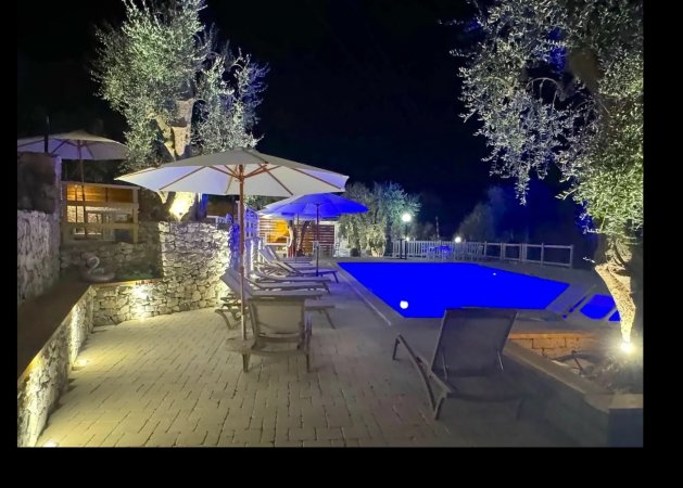 Piscina illuminata di sera con sedie a sdraio e ombrelloni.