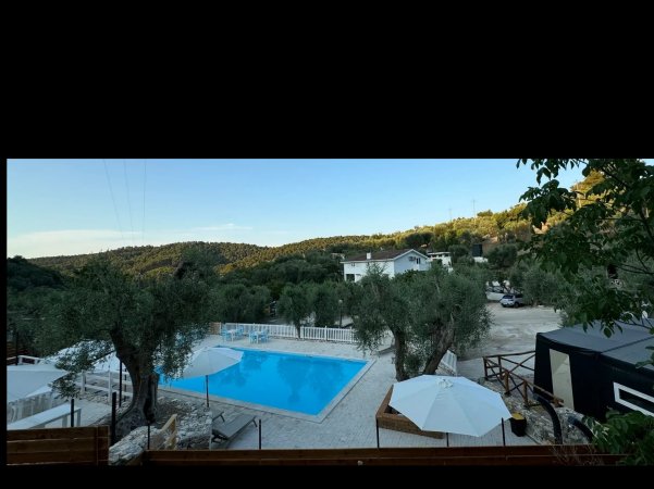 Piscina con vista panoramica su colline alberate e ombrelloni bianchi.