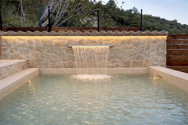 Piscina con cascata su muro di pietra.