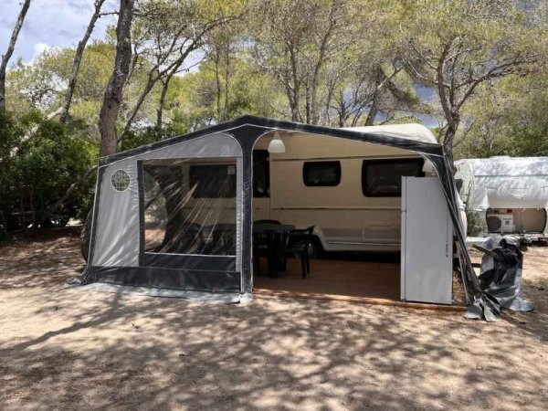 Una roulotte con veranda in un'area ombreggiata da alberi.