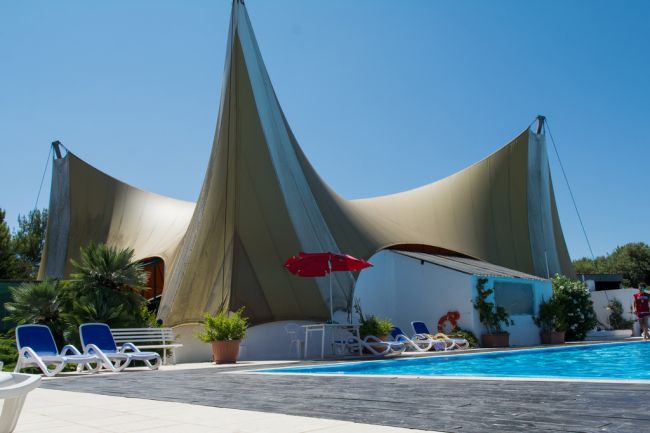 Piscina con struttura di tende a picco e lettini.