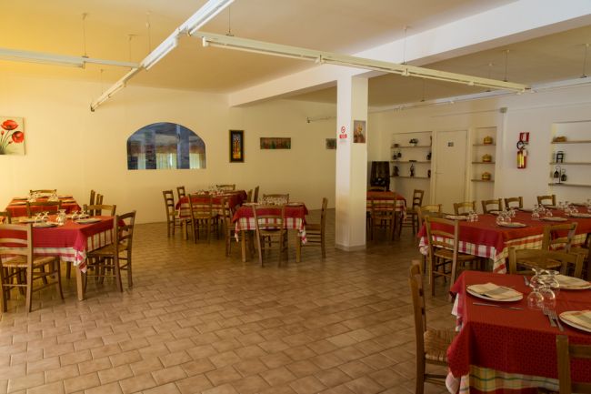 Sala pranzo con tavoli apparecchiati e sedie in legno.