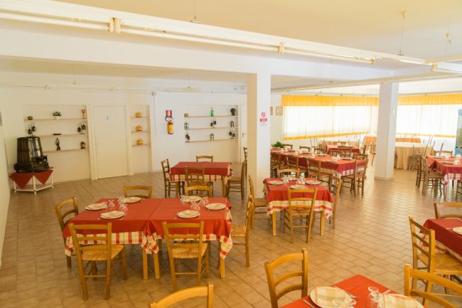 Sala da pranzo con tavoli apparecchiati e sedie di legno.