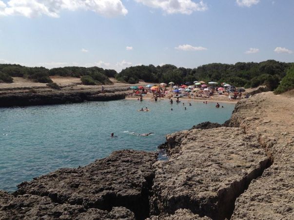 Cala rocciosa con mare cristallino e bagnanti.