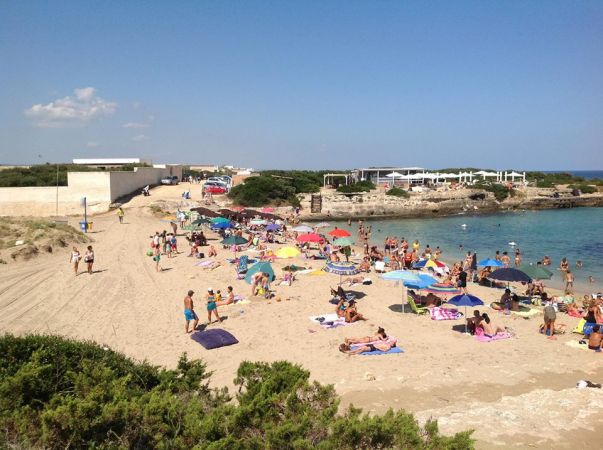 Spiaggia affollata di bagnanti e ombrelloni colorati.