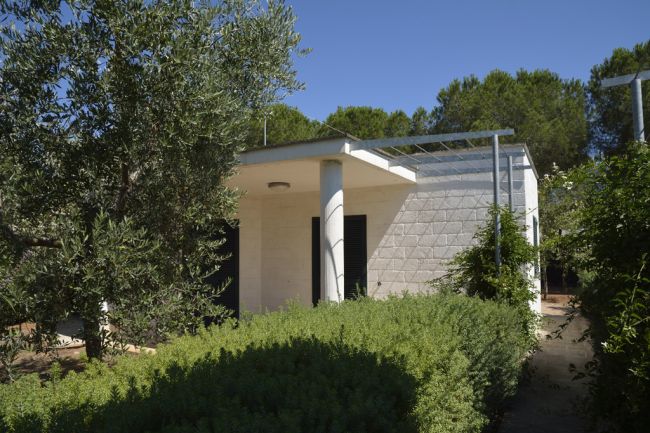 Casa bianca con pilastri, circondata da verde.