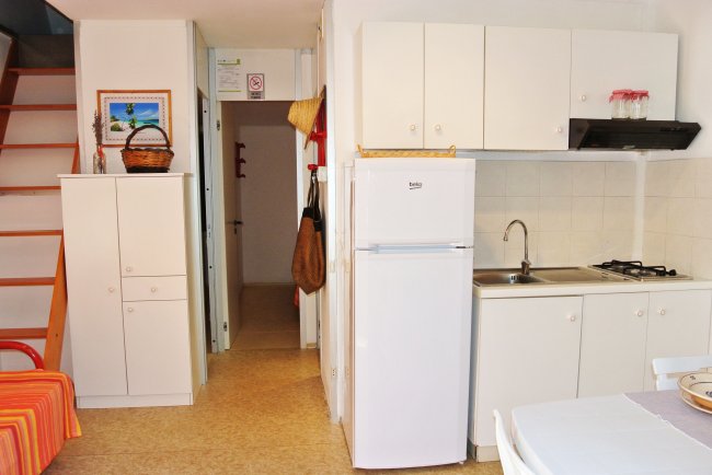 Piccola cucina con frigorifero e mobili bianchi.
