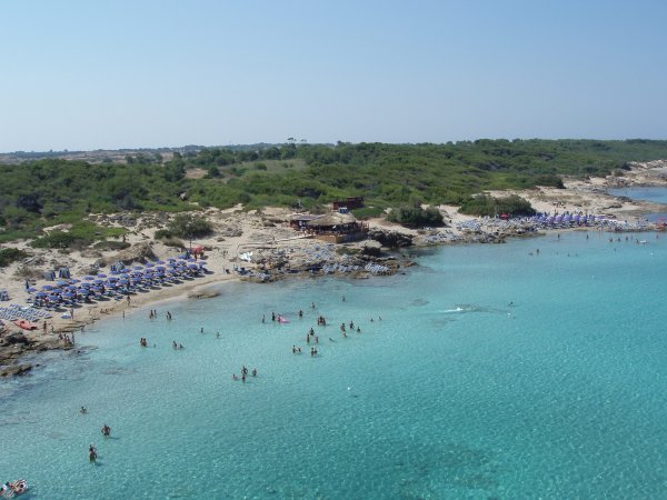 Spiaggia affollata con acqua cristallina e ombrelloni blu.