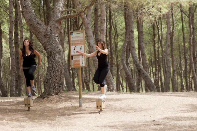 Due persone fanno esercizi su attrezzature in un bosco.