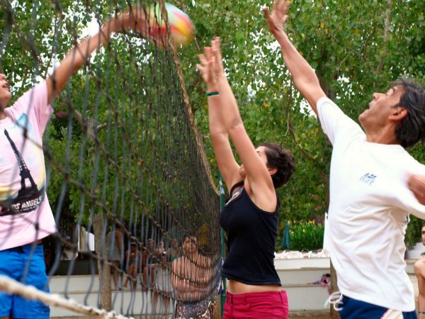 Partita di pallavolo con tre persone che saltano attorno alla rete.