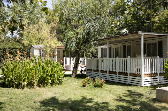 Bungalow con veranda tra alberi e prati verdi.