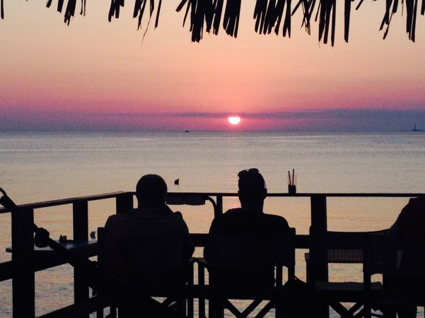 Due persone guardano un tramonto sul mare.