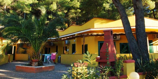 Edificio giallo con verande, circondato da piante e alberi.