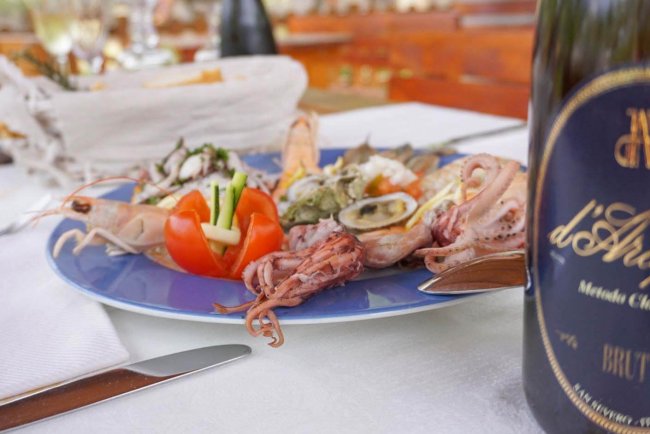 Piatto di frutti di mare e bicchiere di vino su un tavolo apparecchiato.