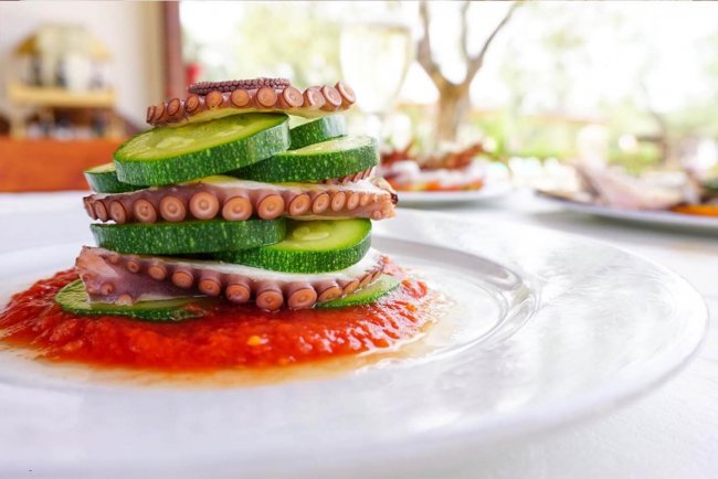 Fette di polpo e zucchine su salsa rossa in un piatto.