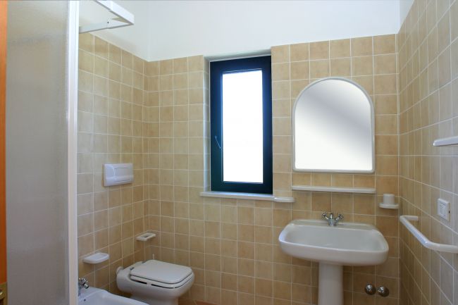 Bagno con piastrelle beige, finestra e specchio.
