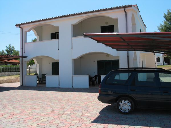 Edificio bianco a due piani con veranda e auto parcheggiata.
