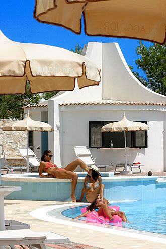 Persone rilassate vicino a una piscina con ombrelloni.
