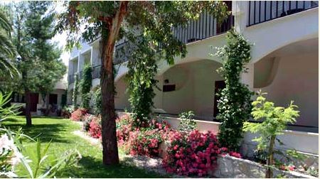 Edificio bianco con balconi e giardino verde, fiori rosa e piante rampicanti.