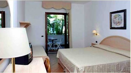 Camera da letto con letto matrimoniale e balcone con sedie bianche.