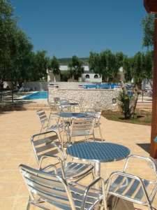 Tavoli e sedie in metallo su una terrazza con vista su una piscina e giardino.