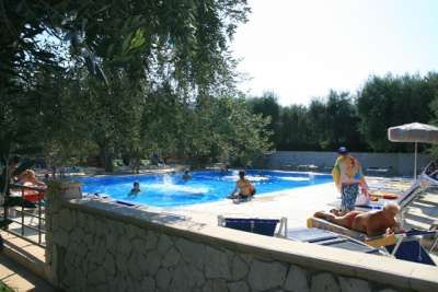Piscina all'aperto di giorno con persone che nuotano e prendono il sole.
