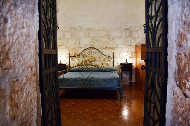 Letto con testiera in ferro battuto, pareti in pietra.