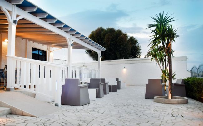 Patio moderno con sedie, accanto a un albero e una pergola bianca.