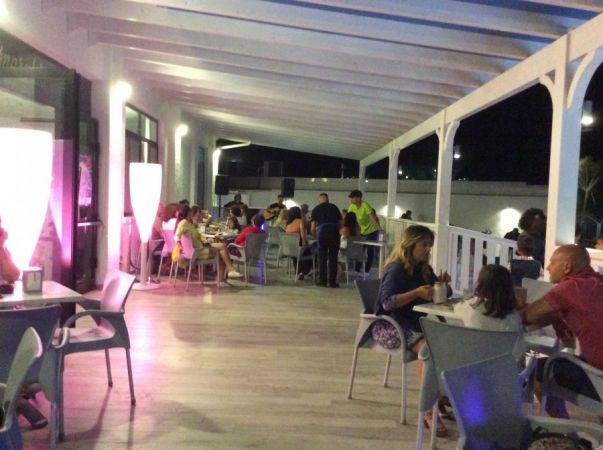 Una terrazza ristorante con persone sedute a tavoli sotto luci soffuse.