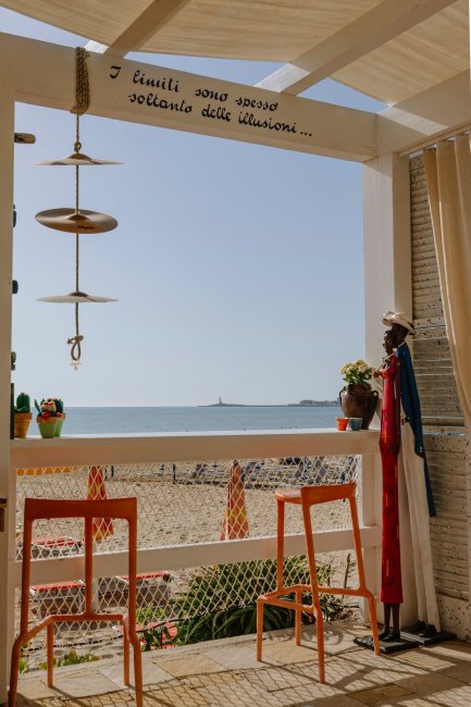 Vista spiaggia da un locale con sgabelli arancioni.