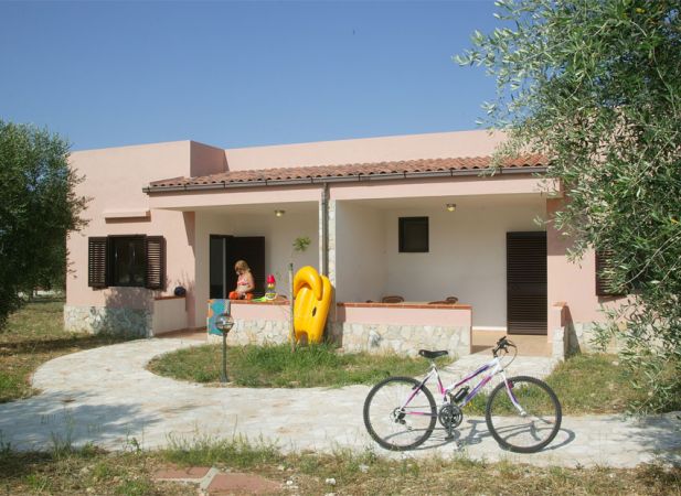 Casa rosa con veranda, giochi da piscina colorati e una bicicletta sul vialetto.
