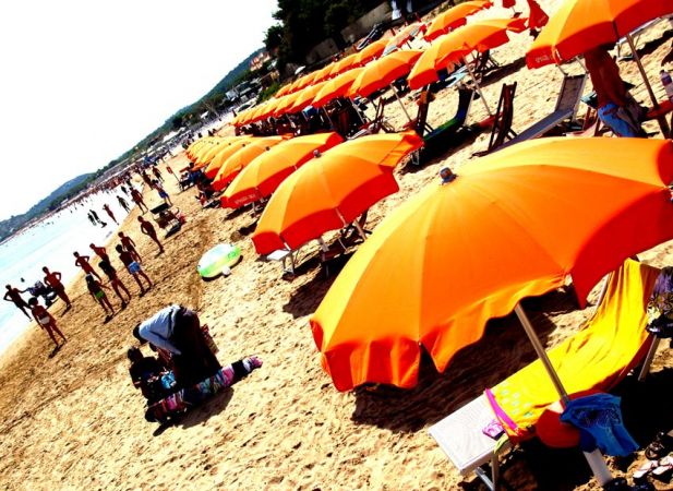 Spiaggia affollata con ombrelloni arancioni e lettini.