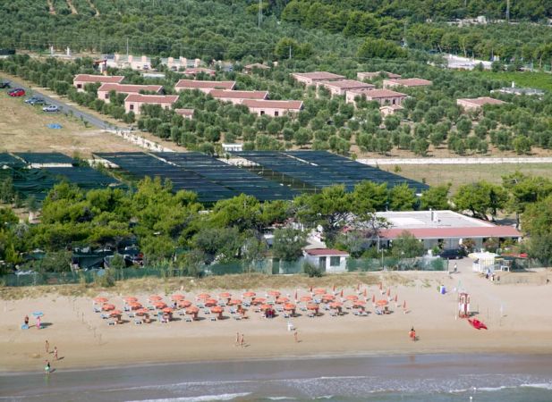 Spiaggia con ombrelloni arancioni, mare e colline con villette.