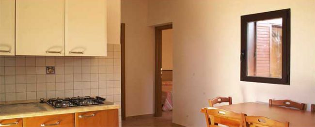 Interno di cucina con fornelli, tavolo e sedie vicino a finestra.