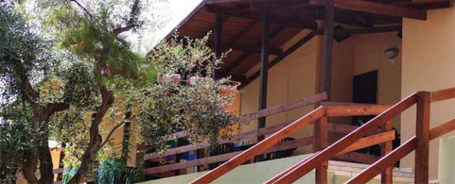 Terrazza di una casa con tettoia in legno e scala in legno tra alberi.