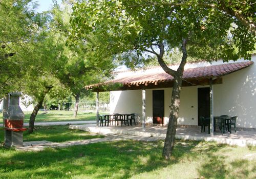 Casa bianca con patio coperto e sedie in un giardino verde.