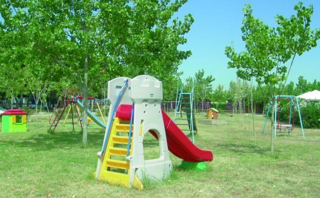 Parco giochi con scivolo, altalene e alberi verdi.