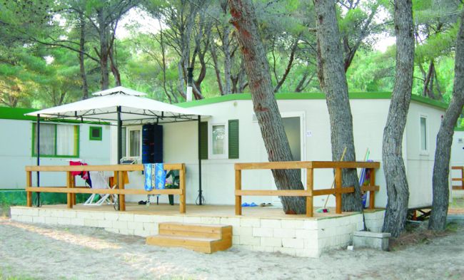 Casa mobile in legno con terrazza immersa nella pineta.